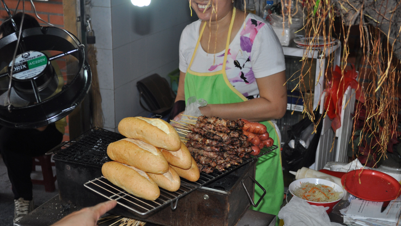 Vietnam street vendor with grilled chicken skewers, pork skewers, and baguettes