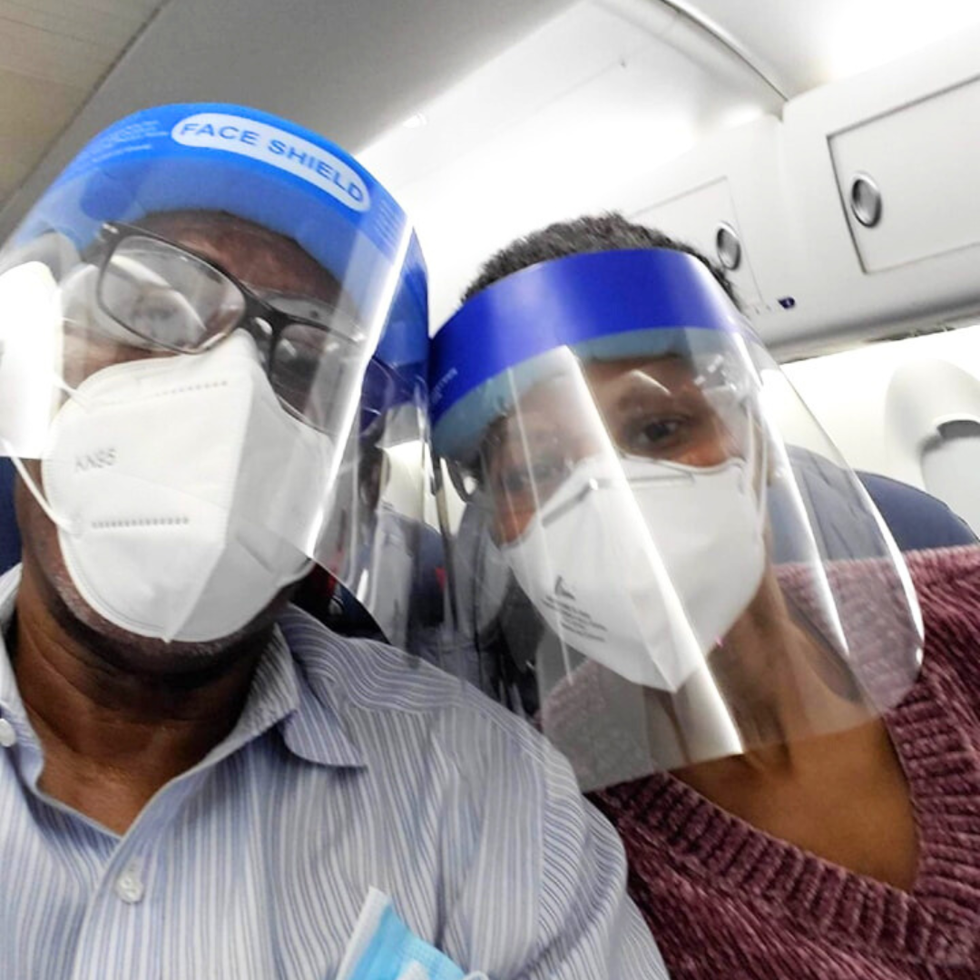 Selfie image of a Black male and Black female wearing N95 masks and face shields while sitting on an airplane.