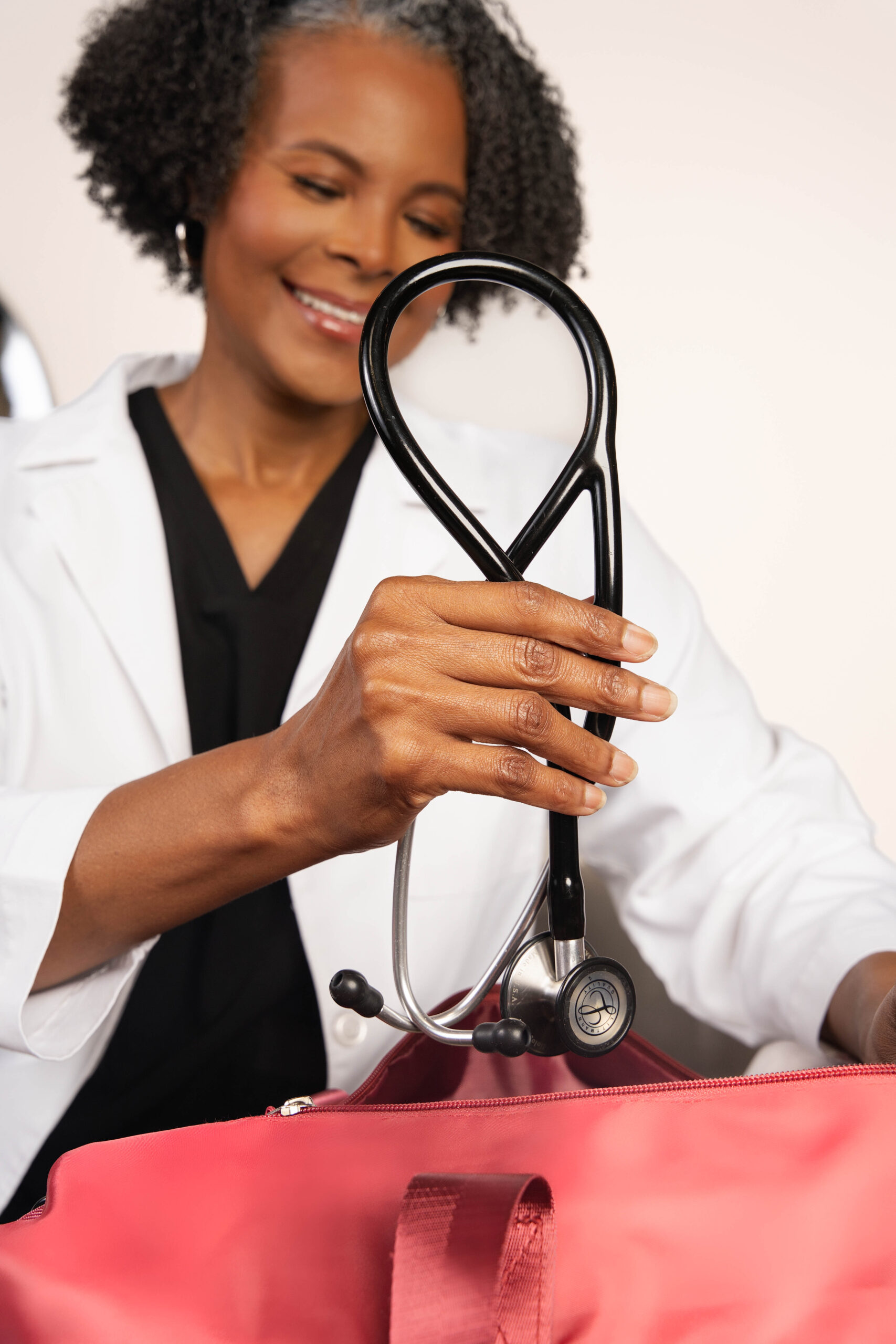 Black female doctor holding a black stethoscope over a red travel bag